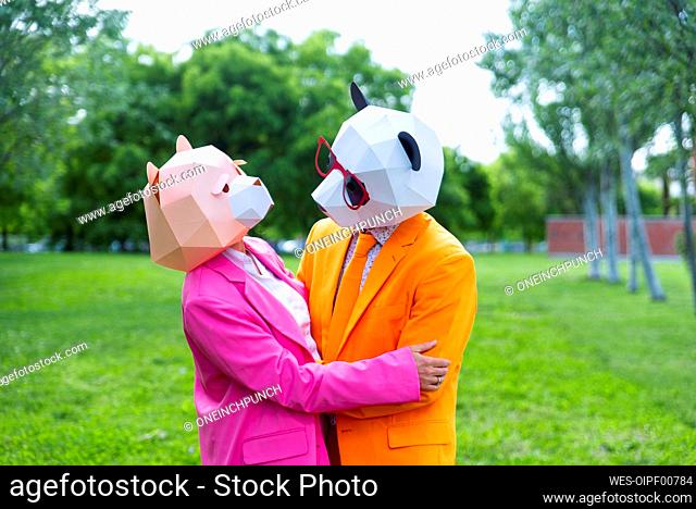 Adult couple¶ÿwearing vibrant suits and animal masks embracing in public park