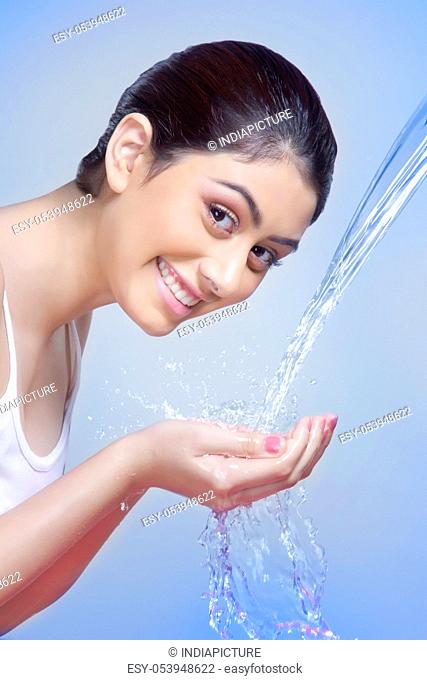 Side view portrait of happy woman washing face against blue background