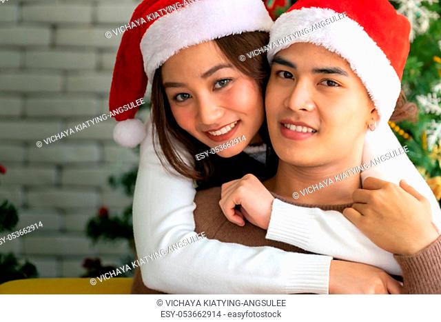 Young asian adult teenager couple hugging and celebrateing christmas holiday together in living room with christmas tree decoration