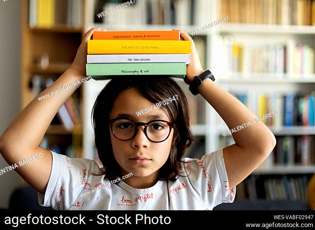 Portrait of serious boy with stack of books on his head