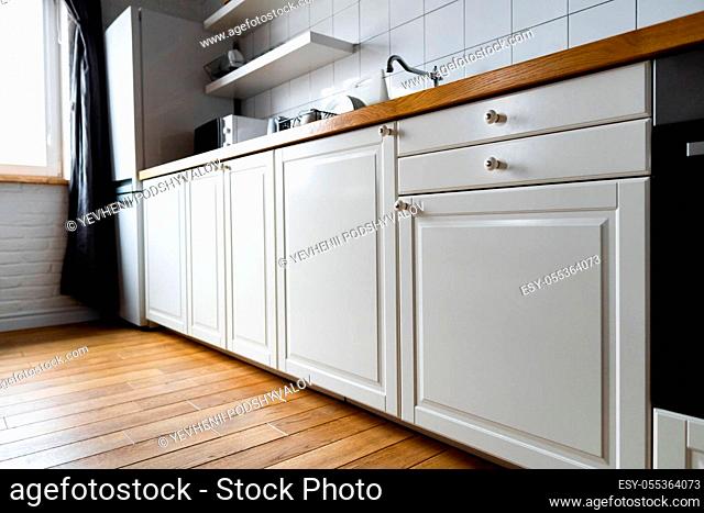 Furniture and appliances: bright white cabinets with wooden countertop, electric cooker, induction hob, faucet, sink and dish rack against hardwood floor and...