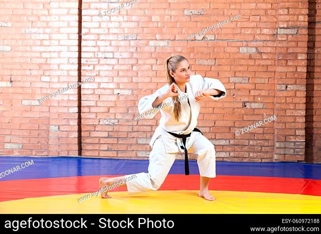 Beautiful athletic karate woman in white kimono with black belt in fighting stance and looking away. Japanese martial arts concept