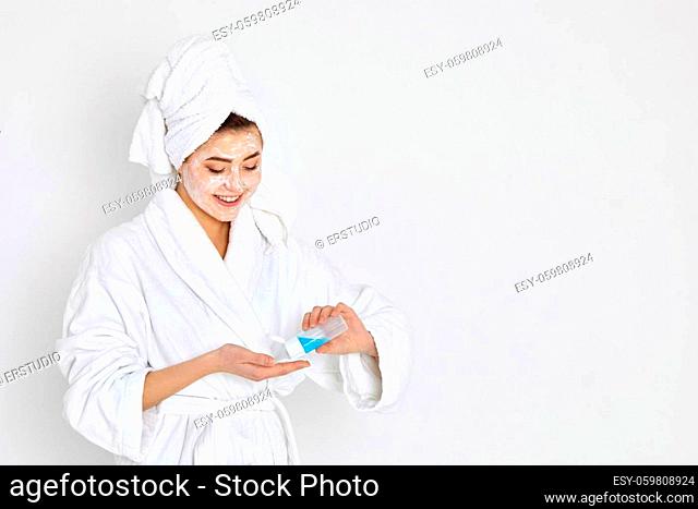woman in white bathrobe with towels on head holds cotton swab and tonic. Skin cleansing. copy space