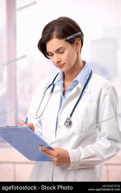 Attractive female doctor standing on hospital corridor doing paperwork