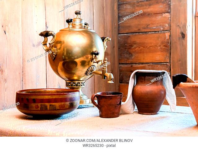 Traditional old copper samovar for tea drinking and ceramic ware on a table in a rural house