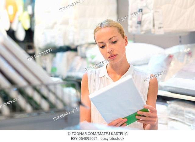 Pretty, young woman choosing the right bed sheets for her bed in modern home furnishings store