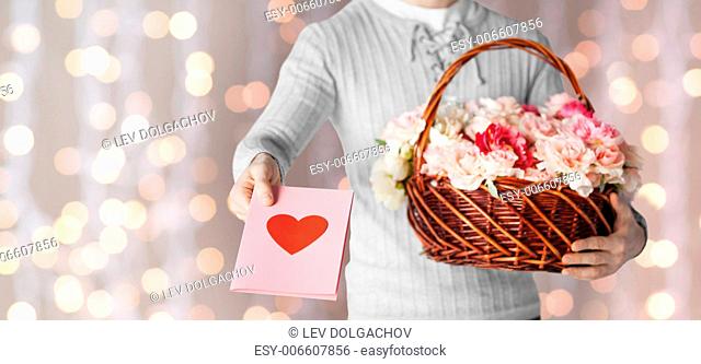 holidays, people, feelings and greetings concept - close up of man holding basket full of flowers and giving postcard over holidays lights background