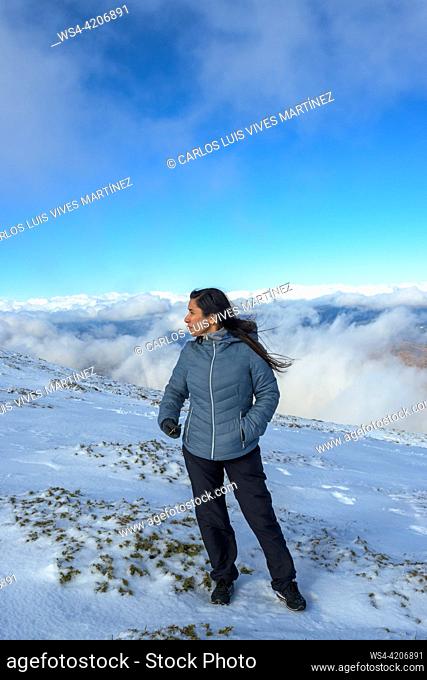 middle-aged latina woman on a snow-capped mountain above the clouds,