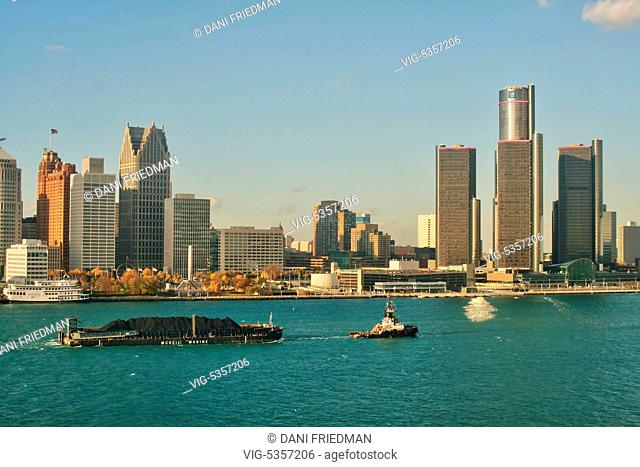 A tugboat pulls a barge loaded with petroleum coke (petcoke) along the Detroit River with the skyline of the city of Detroit, Michigan, USA in the background