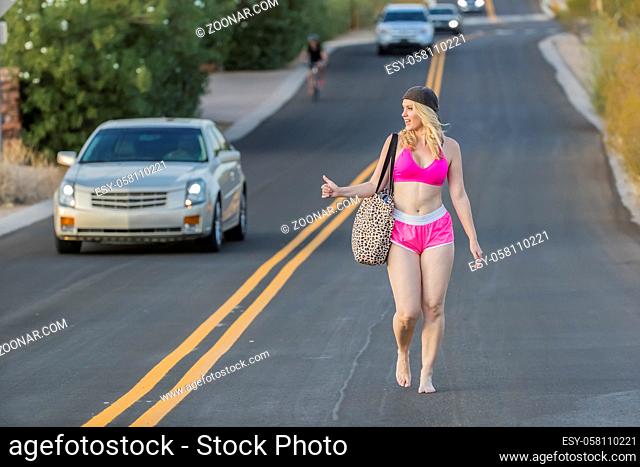 A blonde model walking down the highway hitchhiking