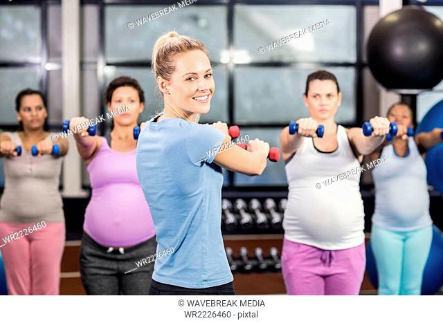 Female trainer with pregnant woman lifting dumbbells