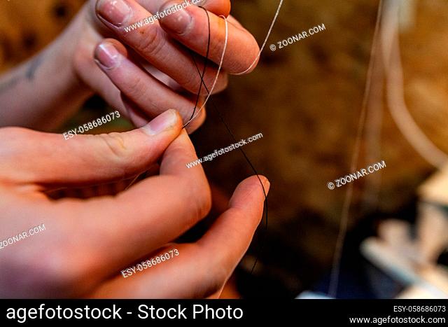 A closeup view on the hands of a tailor tying a knot in black and white threads. Tricky hand work of a creative person in studio