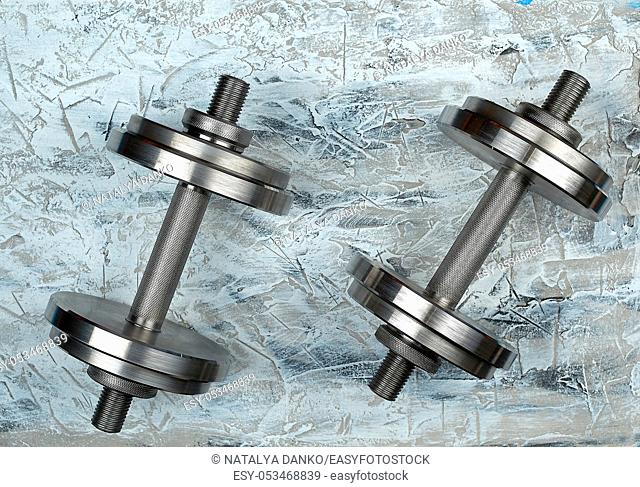 pair of shiny steel typesetting dumbbells for bodybuilding on a gray background, top view