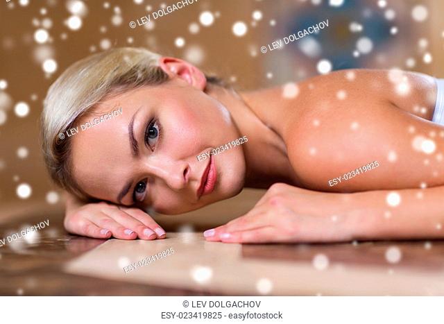 people, beauty, spa, healthy lifestyle and relaxation concept - beautiful young woman lying on hammam table in turkish bath with snow effect