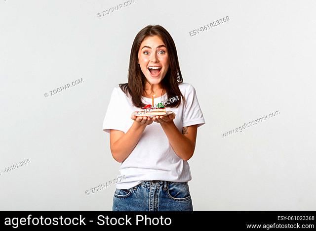 Excited attractive brunette b-day girl making wish on birthday cake, white background
