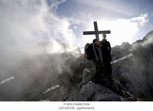 Hikers at a summit cross amidst some clouds, Wetterstein, Bavaria, Germany, Europe