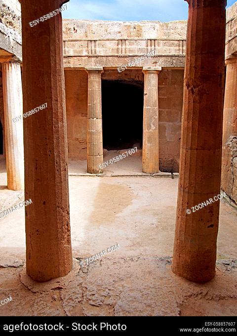 an underground chamber at the tombs of the kings in paphos cyprus with old eroded sandstone columns surrounding a dark empty doorway and blue sky