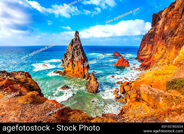 The blinding midday sun illuminates the rocky shore. Madeira is a magical island in the Atlantic. The sharp red rocks, boiling turquoise surf