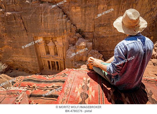 Tourist with sun hat sitting on carpet, looking from above into the gorge Siq, Pharaoh's treasure house carved into rock