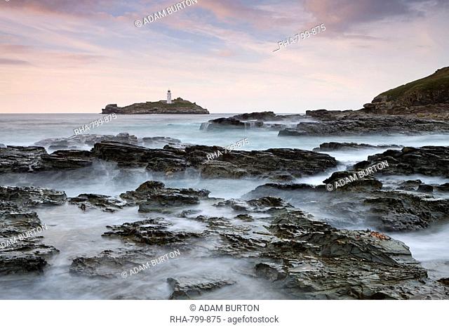Waves crash over the rocks of Godrevy Point at sunset, looking towards Godrevy Lighthouse, Cornwall, England, United Kingdom, Europe