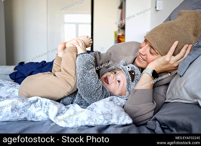 Happy boy playing with mother on bed at home