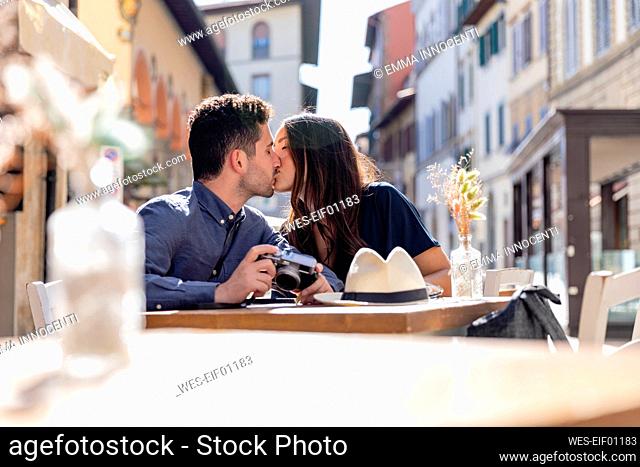 Tourist couple kissing each other at sidewalk cafe