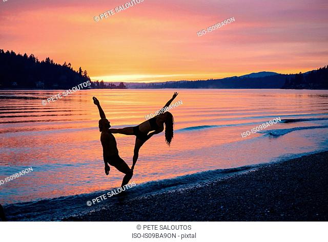 Couple practising yoga on beach at sunset