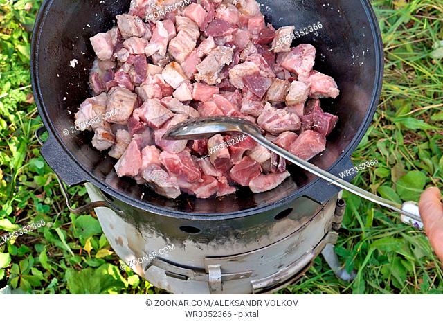 Fast stirring of meat during roasting in a cast-iron bowler at the stake. Outdoor closeup shot