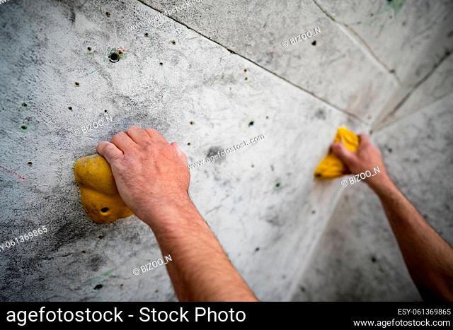 Close up shot of a male hands smeared with magnesium powder grabbing a hold of a climbing wall, at the gym