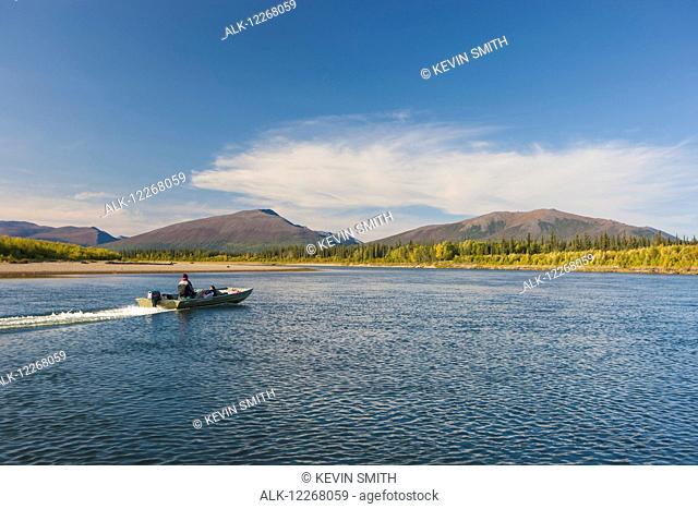 Person driving a small motor boat down the Kobuk river on a calm sunny day, Arctic Alaska, summer