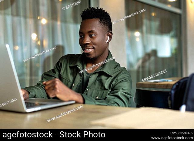 Cheerful young african american man in headphones using computer in cafe