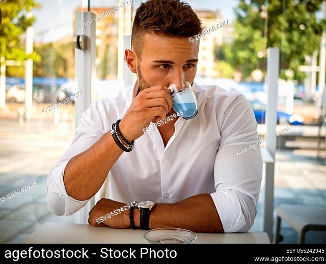 Attractive Young Man Drinking Novelty Blue Coffee while Sitting in a Bar with Serious Expression