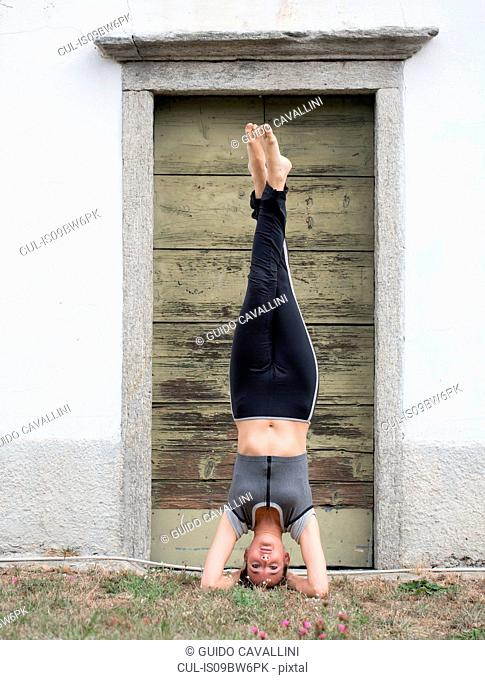Woman practicing yoga, upside down in front of doorway, portrait