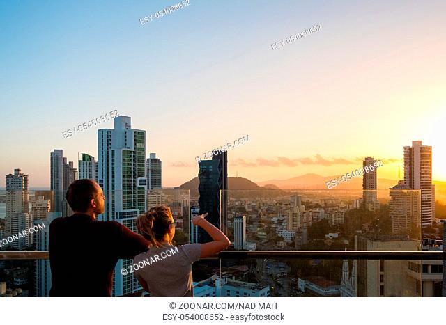 couple looking above city skyline with sunset sky from skyscraper bilding