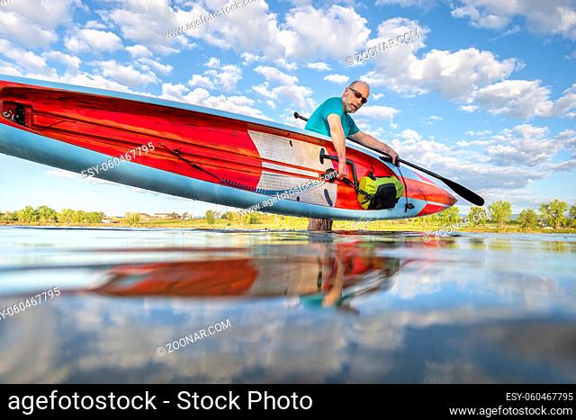 senior male paddler is finishing his morning paddling workout on a racing stand up paddleboard, solo paddling as fitness and training with social distancing