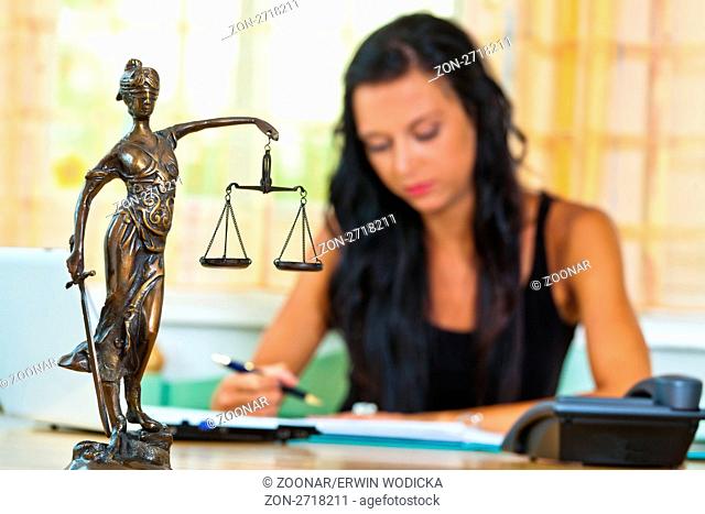 Eine erfolgreiche Rechtsanwältin im Büro mit Justitia Figur im Vordergrund