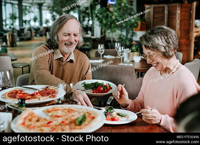 Happy senior man serving food to woman at cafe