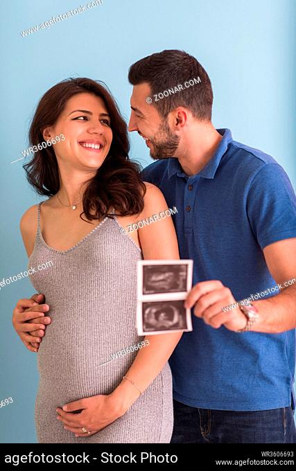 happy pregnant couple looking ultrasound picture of their unborn baby, isolated on blue background