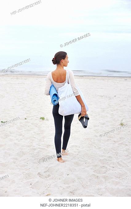 Young woman with exercise mat standing on beach