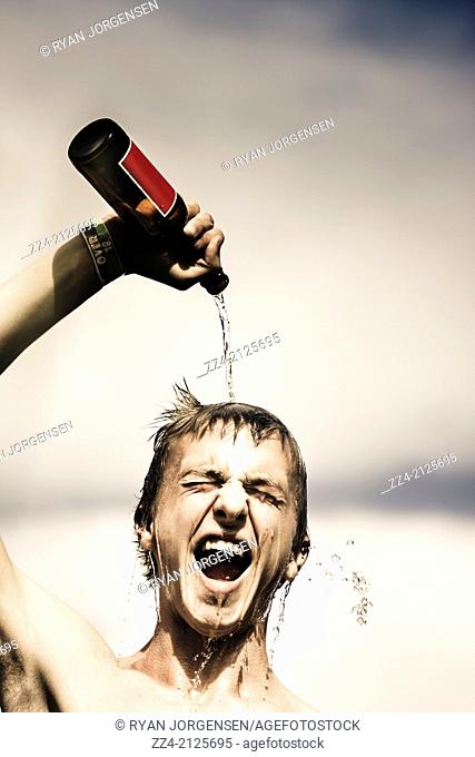 Crazy Irish lifestyle picture of a young man with open mouth smile pouring beer from bottle on head at St Patrick’s Day celebrations