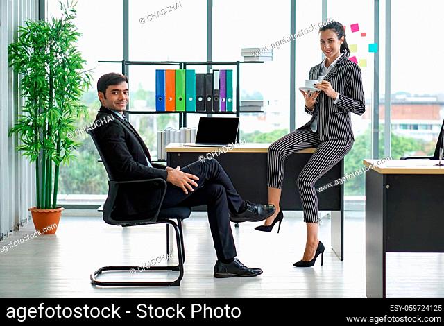 Coffee break atmosphere in a modern office. The manager in a suit rests relax on a chair while his colleagues are drinking coffee