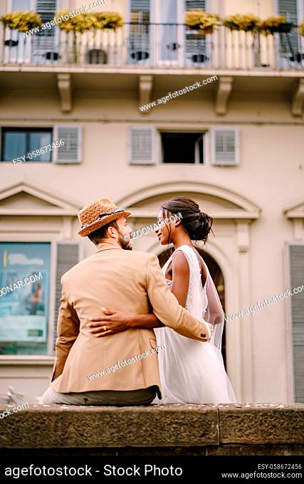 African-American bride in a white dress with a long veil and bouquet, and Caucasian groom in a sand jacket and straw hat. Interracial wedding couple