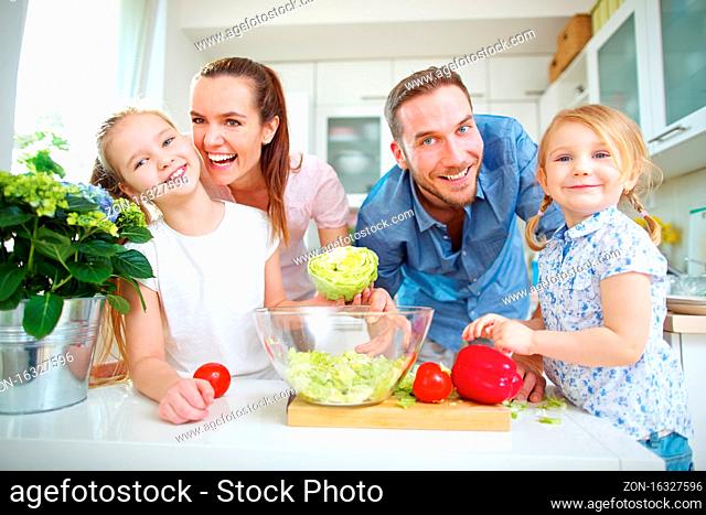Glückliche Familie lebt vegan und steht mit frischem Gemüse in der Küche