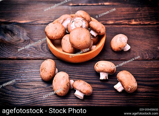 Fresh mushrooms champignons in a wooden bowl on a brown table