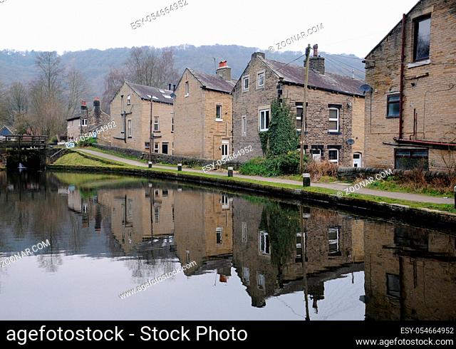 houses alongside the rochdale canal in hebden bridge with reflections in the water and lock gates in the distance