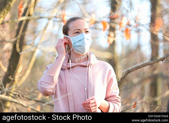 Portrait of caucasian sporty woman wearing medical protection face mask while walking in park, relaxing and listening to music