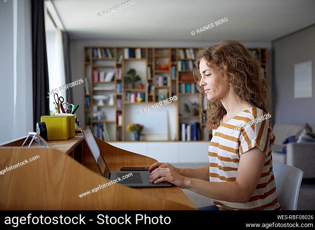 Woman working on laptop while sitting by desk at home