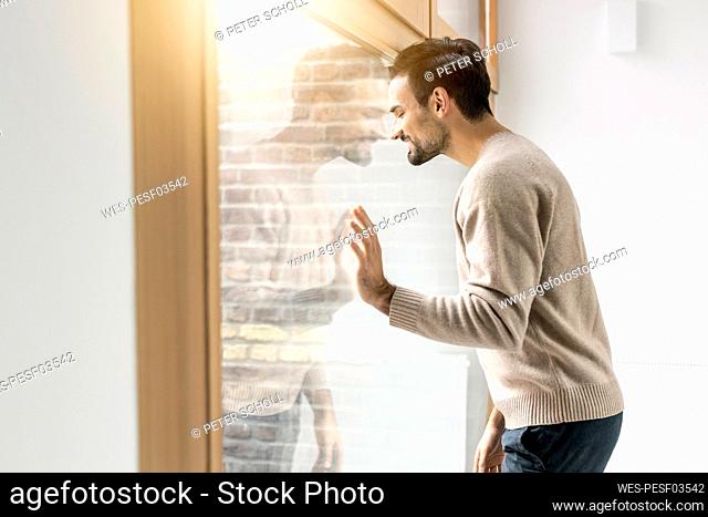 Man with eyes closed leaning on glass window at home