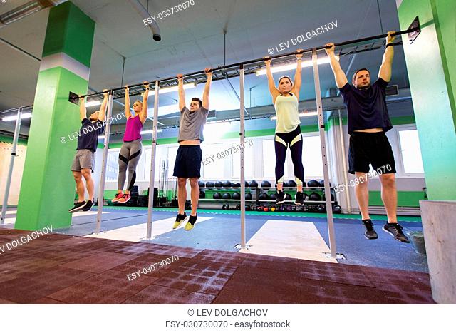 sport, fitness, exercising and training concept - group of people hanging at horizontal bar in gym