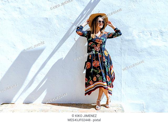 Spain, Cadiz, Vejer de la Frontera, fashionable woman with straw hat standing in front of white wall
